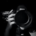 grayscale photo of person holding Canon DSLR